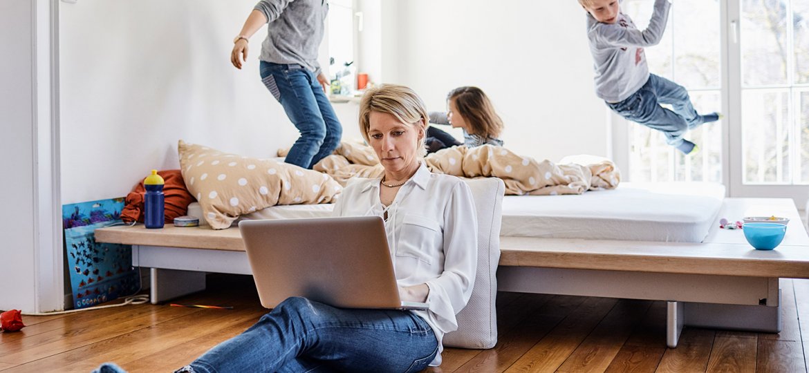 Mother using laptop at home with children romping around in background